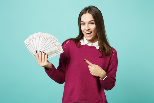 Jonge brunette vrouw meisje in casual kleding poseren geïsoleerd op blauwe achtergrond studio portret. Mensen emoties levensstijl concept. Mock-up kopieerruimte Houd een fan van contant geld in dollarbankbiljetten in de hand