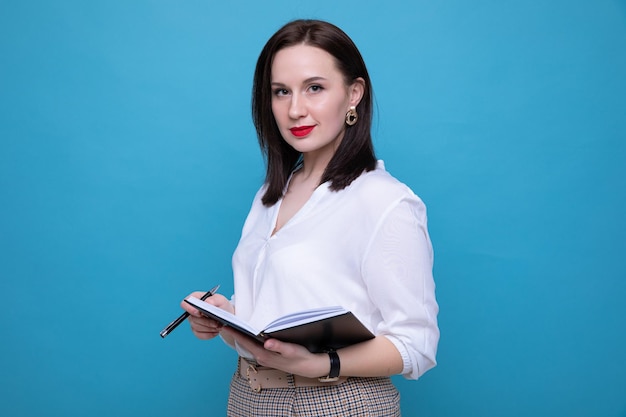 Jonge brunette vrouw met een dagboek en een pen op een blauwe achtergrond