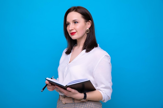 Jonge brunette vrouw met een dagboek en een pen op een blauwe achtergrond