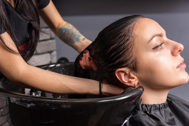 Jonge brunette vrouw met haar gewassen door kapper in wasbak in schoonheidssalon