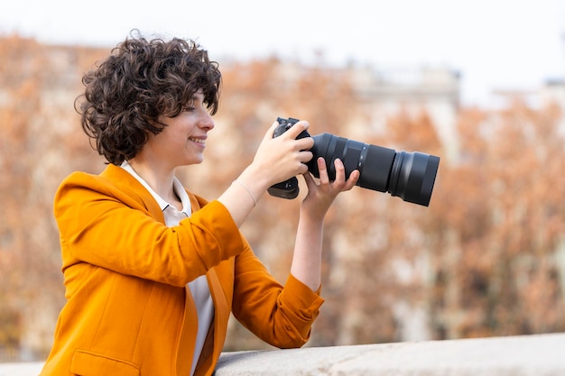 Jonge brunette vrouw met krullend haar die een foto maakt met telelens op straat