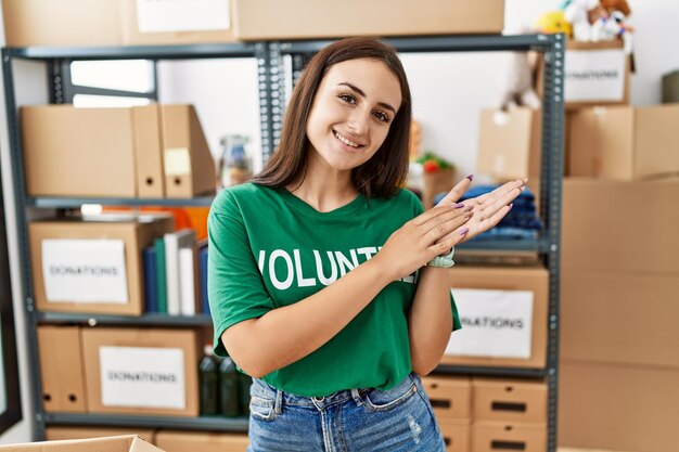 Jonge brunette vrouw met vrijwilligerst-shirt bij donaties staat samen te klappen en te applaudisseren