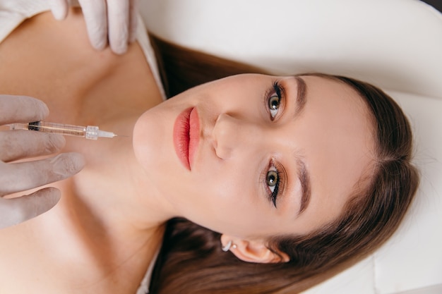 Jonge brunette vrouw plastische chirurgie injectie ontvangen op haar gezicht close-up portret
