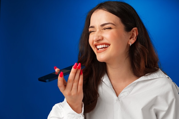 Jonge brunette vrouw praten aan de telefoon tegen blauwe achtergrond