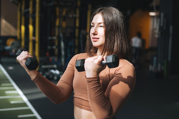 Jonge brunette vrouw traint haar spieren met halters in de sportschool van de fitnessclub