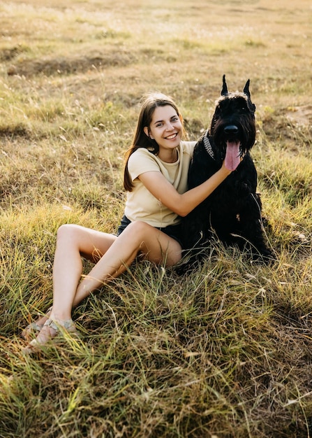 Jonge brunette vrouw zit in een veld en knuffelt haar hond, een reusachtige schnauzer.