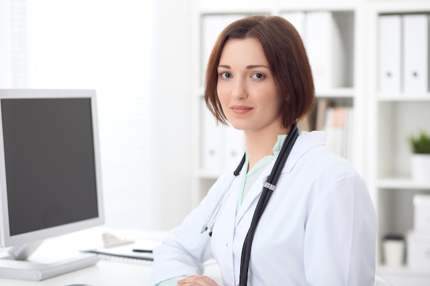 Jonge brunette vrouwelijke arts zit aan een bureau en werkt op de computer op het ziekenhuiskantoor