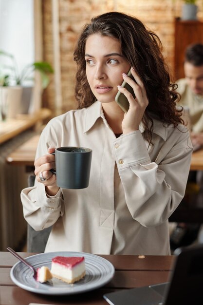 Jonge brunette vrouwelijke freelancer praten op mobiele telefoon voor laptop