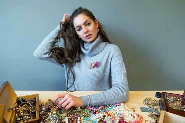 Jonge brunette zit aan tafel met veel sieraden die verschillende sieraden kiezen en proberen