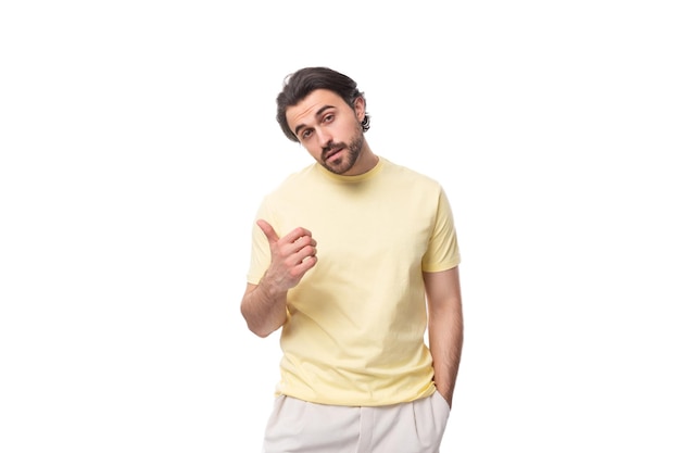 Jonge brute brunette man in een t-shirt wijst zijn hand naar de zijkant op een witte achtergrond met kopie