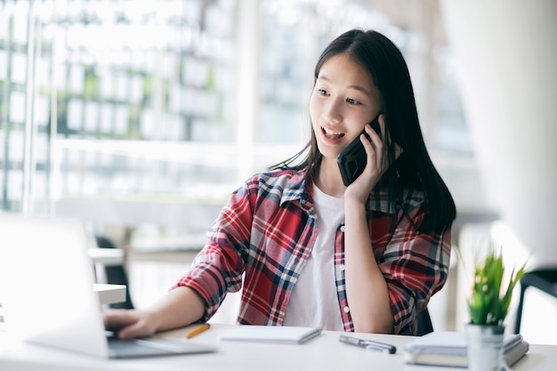 Jonge bureauvrouw die op mobiele telefoon met cliënt spreekt.