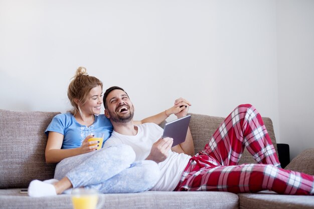 Jonge charmante man en vrouw die van een weekendochtend samen met een tablet genieten terwijl het zitten op de bank in woonkamer.