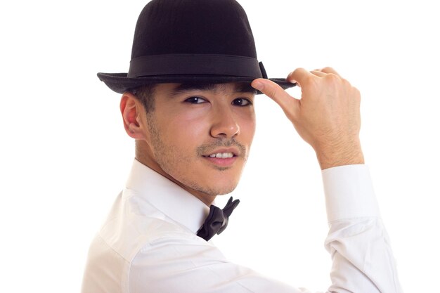 Jonge charmante man in wit overhemd met zwarte vlinderdas en zwarte hoed op witte achtergrond in studio