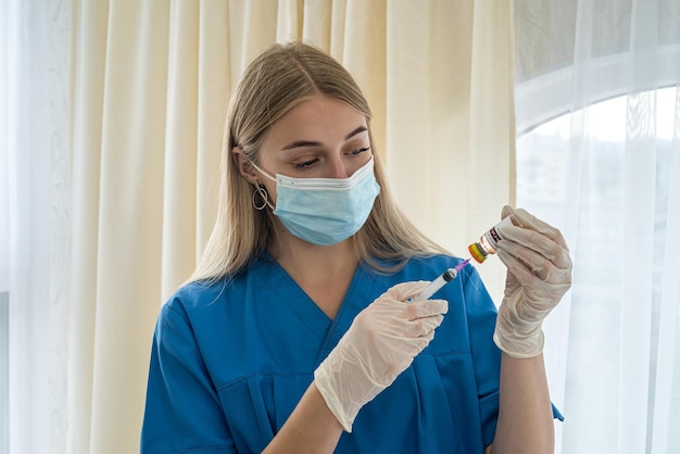 Jonge charmante verpleegster in handschoenen en masker trekt een vaccin met een injectiespuit voor vaccinatie Het concept van het vaccineren van mensen tegen coronavirus