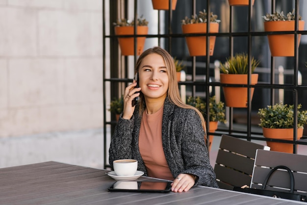 Jonge charmante vrouw belt op een mobiele telefoon terwijl ze alleen in een café zit en praat