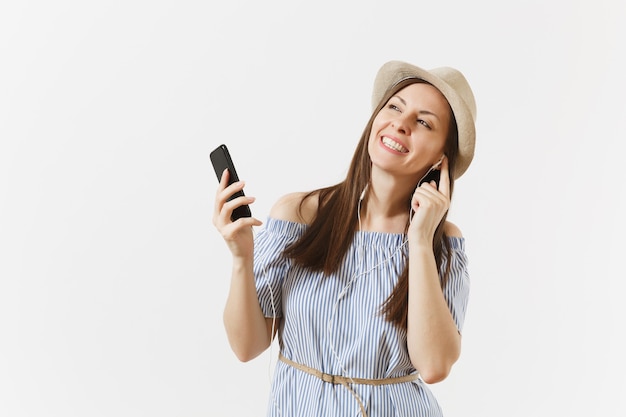 Jonge charmante vrouw in jurk, hoed luisteren muziek in oortelefoons op mobiele telefoon, genieten, ontspannen geïsoleerd op een witte achtergrond. Mensen, oprechte emoties, lifestyle concept. Reclame gebied. Ruimte kopiëren.