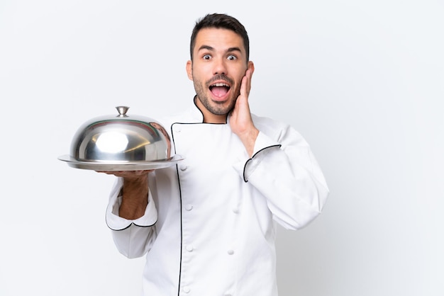 Jonge chef-kok met dienblad geïsoleerd op een witte achtergrond met verrassing en geschokte gezichtsuitdrukking