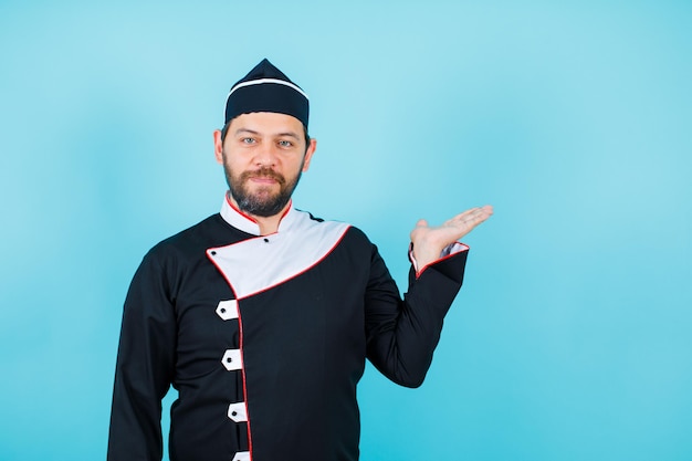 Jonge chef-kok wijst naar rechts met handvol op blauwe achtergrond