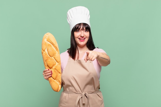 Jonge chef-kokvrouw die naar de camera wijst met een tevreden, zelfverzekerde, vriendelijke glimlach, die jou kiest