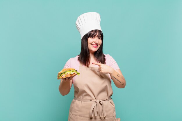 Jonge chef-kokvrouw die vrolijk lacht, zich gelukkig voelt en naar de zijkant en naar boven wijst, een object in de kopieerruimte toont