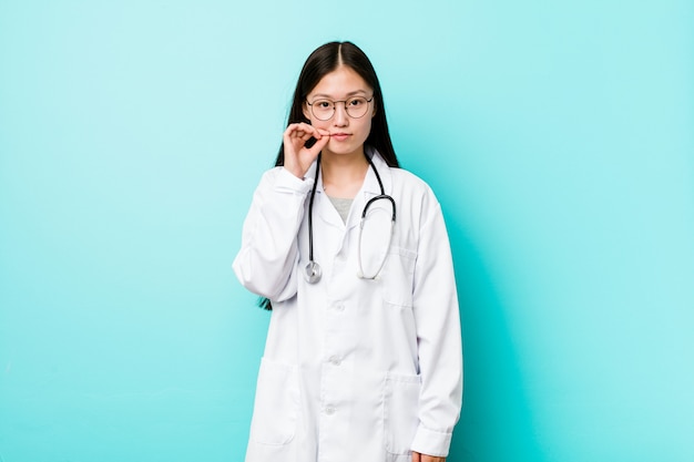 Jonge chinese artsenvrouw met vingers op lippen die een geheim houden.