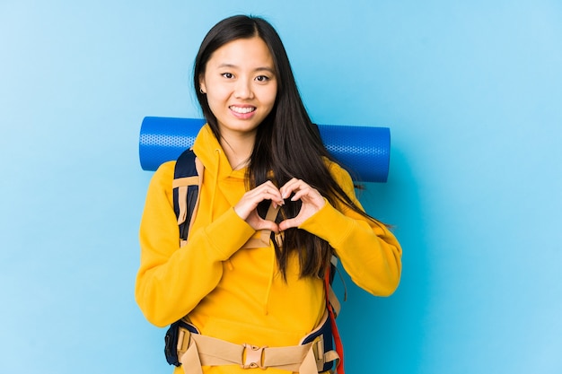 Jonge Chinese backpackervrouw die en een hartvorm met handen glimlacht toont.