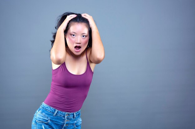 Jonge chinese brunette met haar handen op haar hoofd in shock