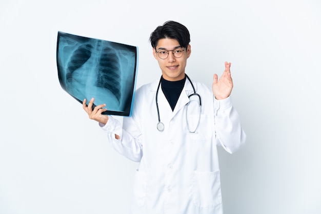 Jonge Chinese doktersmens die radiografie houdt die op witte muur wordt geïsoleerd die met hand met gelukkige uitdrukking groeten