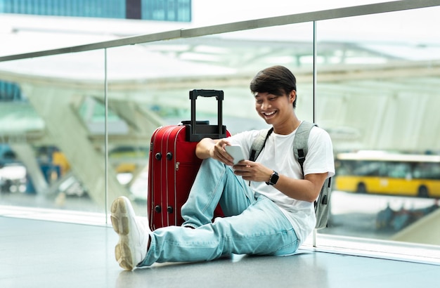 Jonge Chinese man met behulp van mobiele telefoon tijdens het wachten op de vlucht