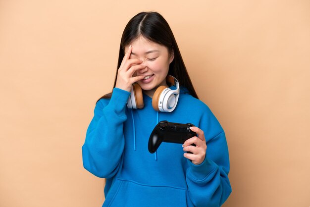 Jonge Chinese man spelen met een video game controller geïsoleerd op beige achtergrond lachen