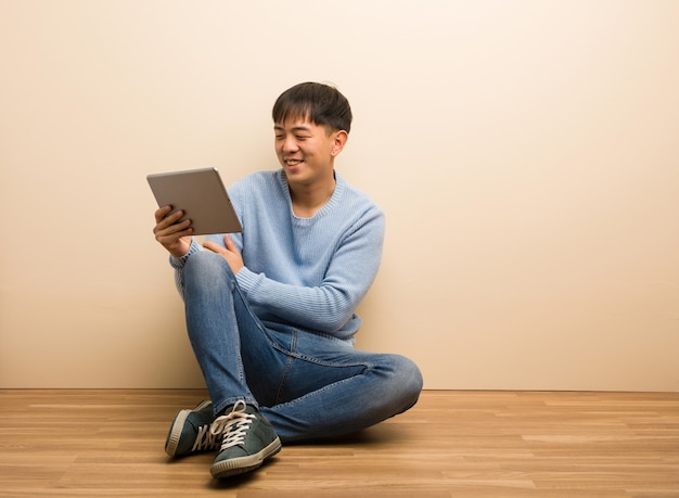 Jonge Chinese mensenzitting die zijn tablet gebruiken die zekere en wapens glimlachen kruisen, die omhoog eruit zien