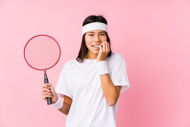 Jonge Chinese vrouw badminton spelen in een roze muur bijten nagels, nerveus en erg angstig.