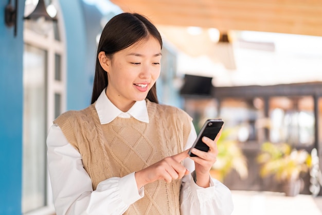 Jonge Chinese vrouw die buitenshuis een bericht of e-mail verzendt met de mobiel