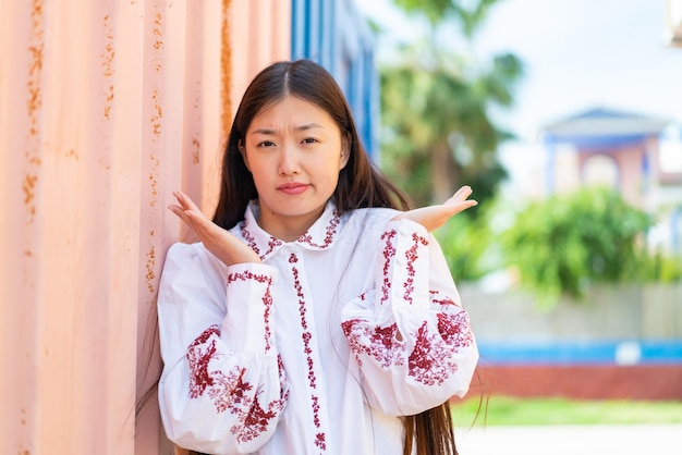 Foto jonge chinese vrouw die buitenshuis twijfels gebaar maakt