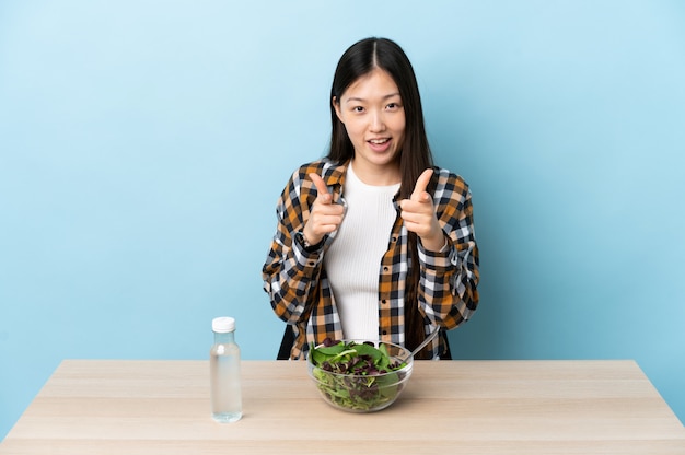 Jonge Chinese vrouw die een aan de voorzijde richt en salade eet die glimlacht