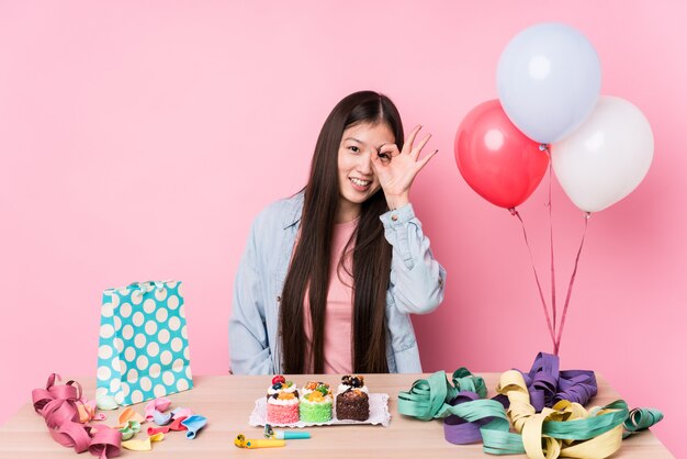 Jonge Chinese vrouw die een geïsoleerde verjaardag organiseert het houden van ok gebaar op oog.