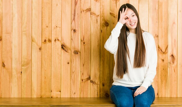 Jonge chinese vrouw die een houten opgewekte plaats zit die ok gebaaroog houdt.