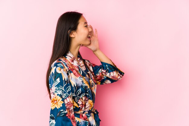 Jonge chinese vrouw die een kimonopyjama draagt die en palm schreeuwt dichtbij geopende mond houdt.