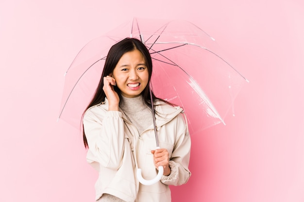 Jonge Chinese vrouw die een paraplu geïsoleerd houdt behandelend oren met handen.