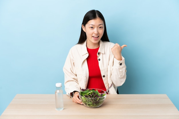 Jonge chinese vrouw die een salade eet die naar de kant wijst om een product te presenteren