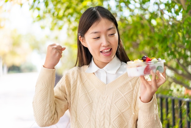 Jonge Chinese vrouw die een schaal met fruit vasthoudt terwijl ze een overwinning viert