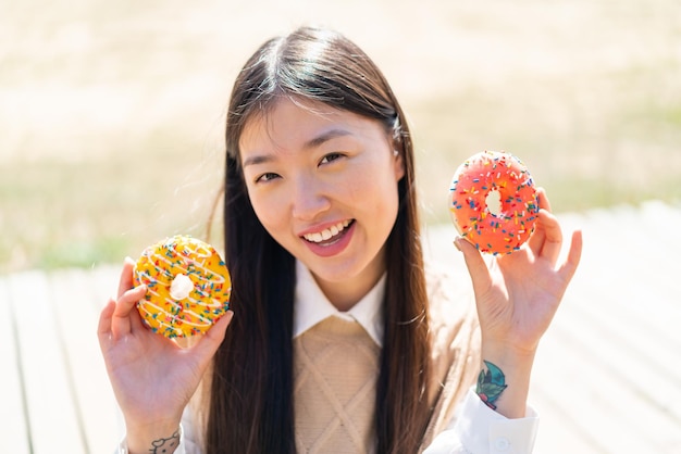 Jonge Chinese vrouw die in openlucht donuts met gelukkige uitdrukking houdt