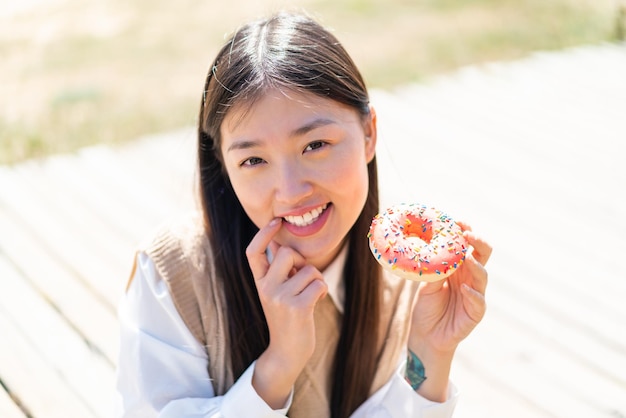 Jonge Chinese vrouw die in openlucht een donut houdt