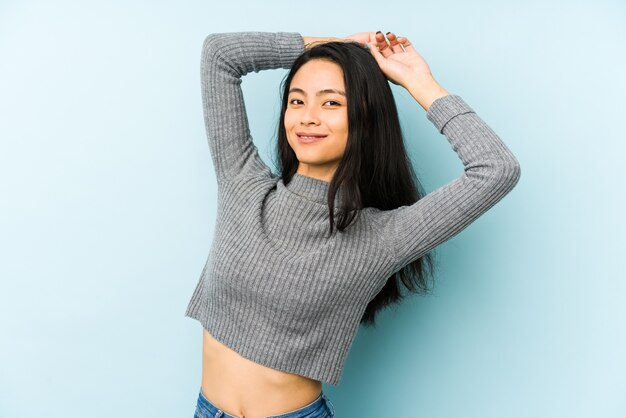 Jonge chinese vrouw die op een blauwe muur wordt geïsoleerd die wapens, ontspannen positie uitrekt.