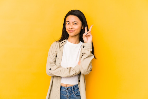 Jonge Chinese vrouw die op een gele muur wordt geïsoleerd die nummer twee met vingers toont.