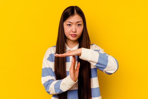 Jonge chinese vrouw die op gele achtergrond wordt geïsoleerd die een onderbrekingsgebaar toont.