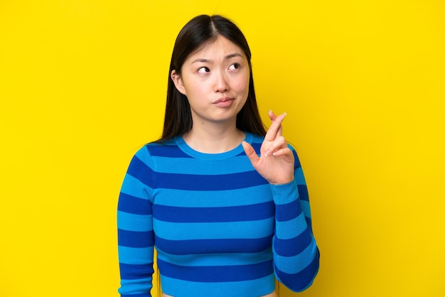 Jonge Chinese vrouw die op gele achtergrond wordt geïsoleerd met vingers die elkaar kruisen en het beste wensen