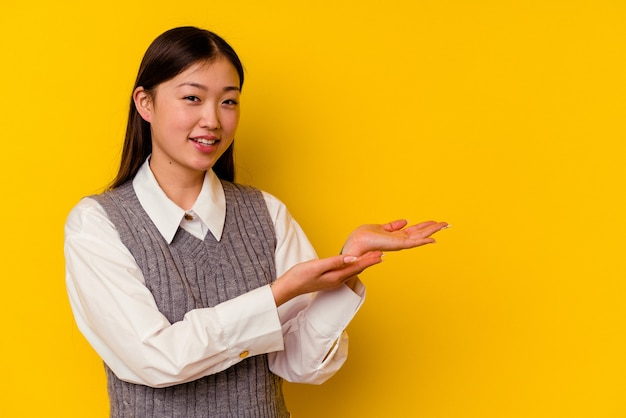 Jonge chinese vrouw die op gele muur wordt geïsoleerd die een exemplaarruimte op een palm houdt.