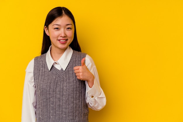 Jonge Chinese vrouw die op gele muur wordt geïsoleerd die en duim opheft