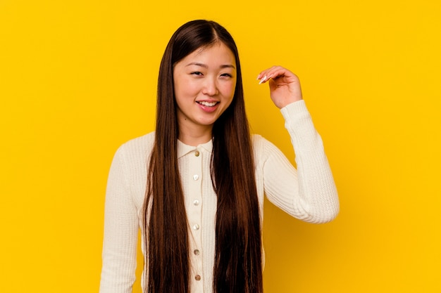 Jonge chinese vrouw die op gele muur wordt geïsoleerd die om iets lacht, die mond behandelt met handen